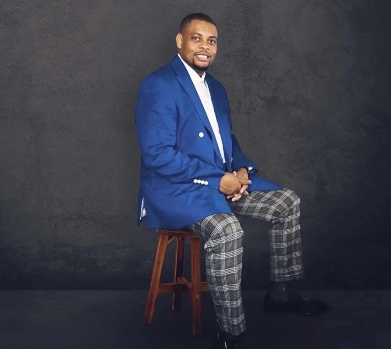 Bishop EW Muir in a blue blazer, seated on a stool